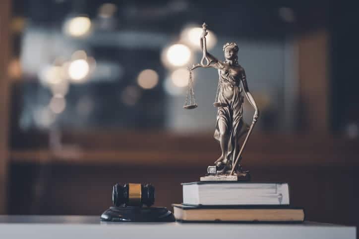 A Lady Justice statue on top of a stack of books with a gavel next to it. 