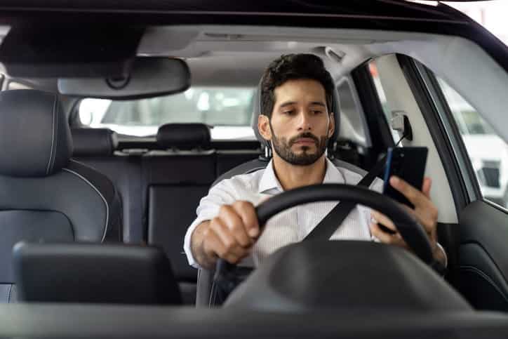 A rideshare driver on his phone, looking to see his next pickup while behind the wheel of his car. 