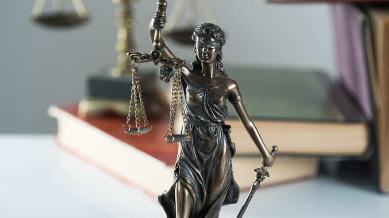 A Lady Justice statue in front of a stack of books and the scales of justice. 