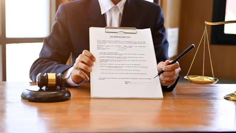 A car accident lawyer reviewing a contract agreement with a client. Next to them is the scales of justice and a gavel.