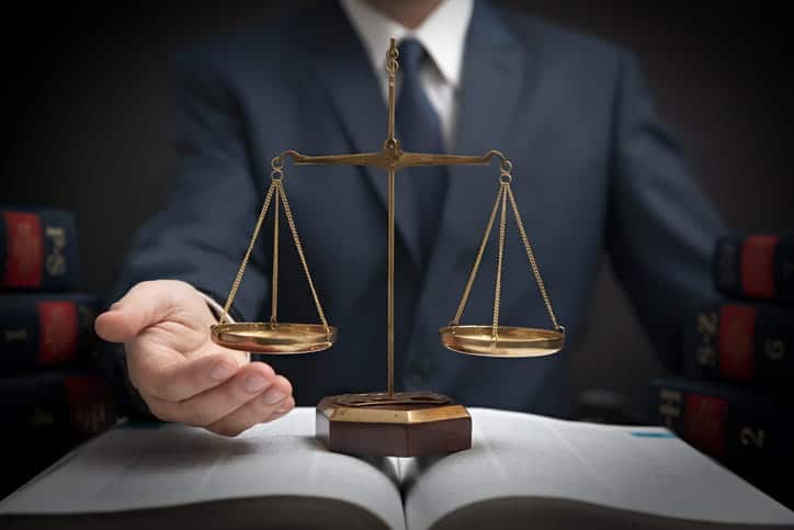 A personal injury attorney holding a hand under the scales of justice as it rests on top of a law book. 